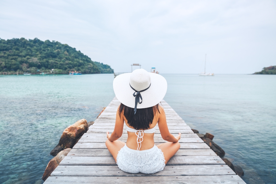 אישה עם כובע לבן יושבת על דק מול הים.