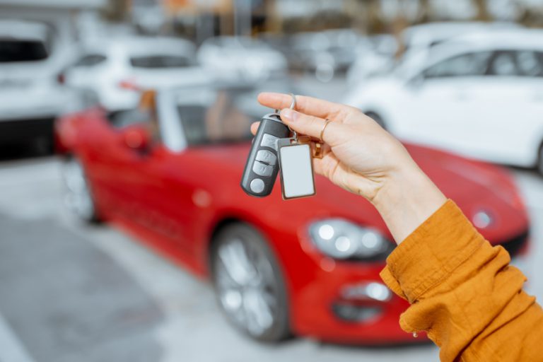 יד של אדם מחזיקה מפתחות של רכב חדש. ברקע רואים אוטו ספורט אדום.